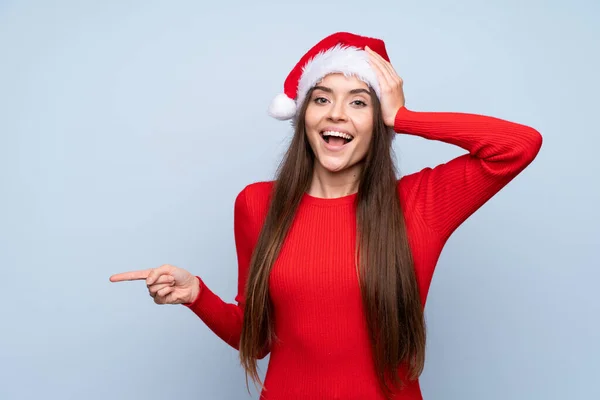 Meisje Met Kerst Hoed Geïsoleerde Blauwe Achtergrond Verrast Wijzend Vinger — Stockfoto