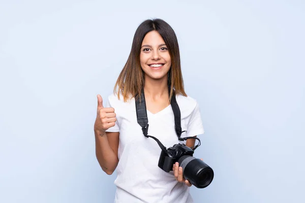 用专业相机和大拇指在孤立的蓝色背景上的年轻女子 — 图库照片