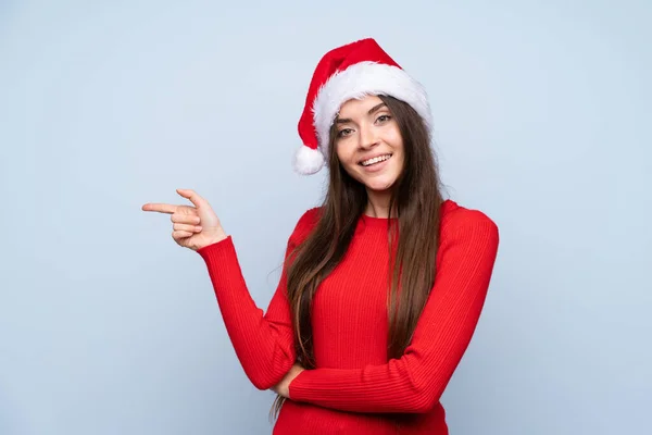 女の子とともにクリスマス帽子以上隔離された青の背景指差し指へザサイド — ストック写真