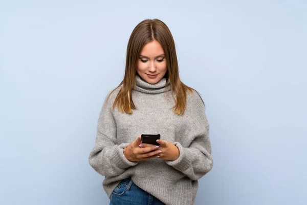 Menina Adolescente Com Suéter Sobre Fundo Azul Isolado Usando Telefone — Fotografia de Stock