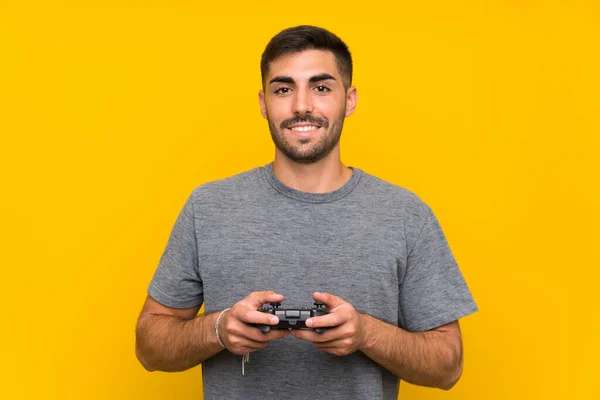 Joven hombre guapo jugando con un controlador de videojuegos sobre fondo amarillo aislado —  Fotos de Stock