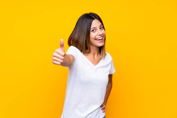 Young woman over isolated yellow background with thumbs up because something good has happened