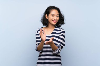 Asyalı genç bir kadın, bir konferansta sunumdan sonra mavi arka planda alkışlıyor.