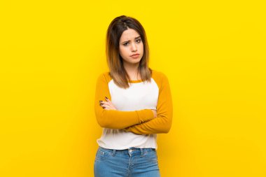 Güzel genç bir kadın, izole edilmiş sarı duvarda üzgün.