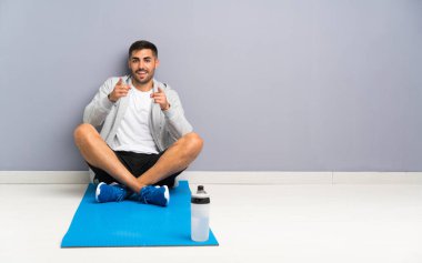 Sport man sitting one the floor points finger at you