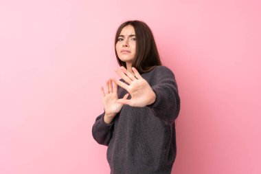 Soyutlanmış pembe arka planda genç bir kadın gergin ellerini öne uzatıyor.