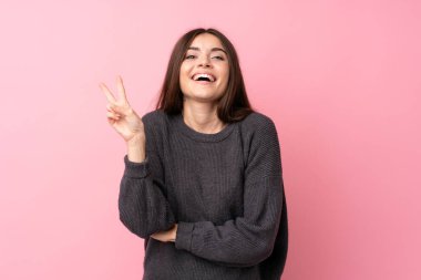 Soyutlanmış pembe arka planda genç bir kadın gülümsüyor ve zafer işareti gösteriyor