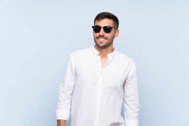 Gözlüklü ve mutlu, mavi arka planda sakallı yakışıklı bir adam.