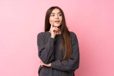 Soyutlanmış pembe arka planı olan genç bir kadın yukarı bakarken bir fikir düşünüyor.