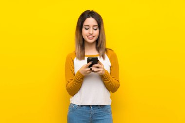 İzole sarı duvar üzerinde güzel genç kadın mobil bir mesaj gönderme