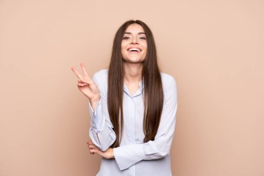 Arka planda kalmış genç bir kadın gülümsüyor ve zafer işareti gösteriyor.