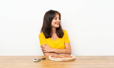 Elinde pizza olan beyaz bir kız yan tarafa bakıyor.