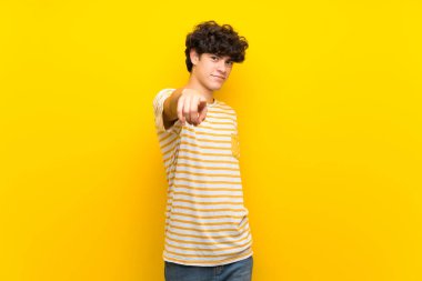 Aşırı izole edilmiş sarı duvarlı genç adam, kendini beğenmiş bir ifadeyle seni işaret ediyor.