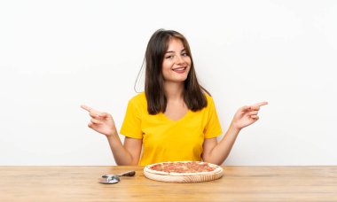 Elinde pizza olan beyaz bir kız yan tarafı işaret ediyor. Şüpheleri var.