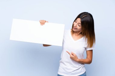 İzole edilmiş mavi arka plan üzerinde genç bir kadın bir konsept eklemek için boş beyaz bir levha tutuyor.