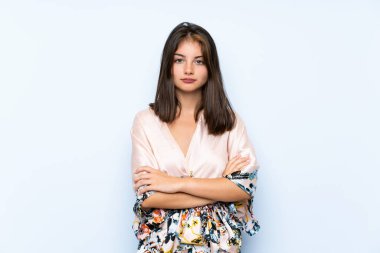 Kimonosu olan beyaz bir kız izole edilmiş mavi arka planda kollarını kavuşturuyor.