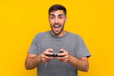 İzole sarı arka plan üzerinde bir video oyunu denetleyicisi ile oynayan genç yakışıklı adam
