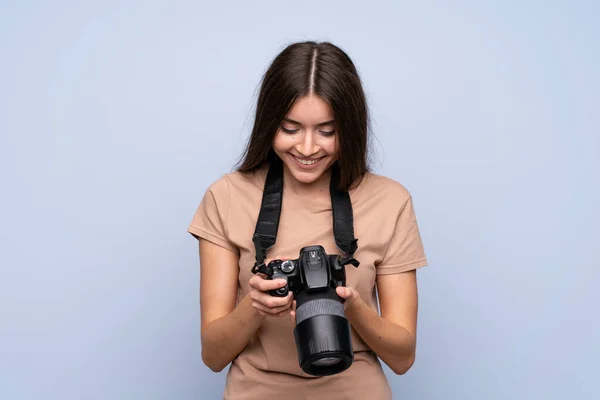 Jovem Mulher Sobre Fundo Azul Isolado Com Uma Câmera Profissional — Fotografia de Stock