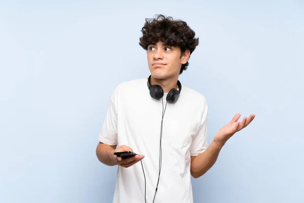 Joven Escuchando Música Con Móvil Sobre Una Pared Azul Aislada —  Fotos de Stock