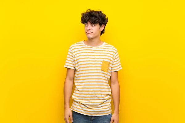 Young man over isolated yellow wall making doubts gesture looking side