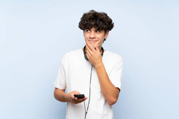 Joven Escuchando Música Con Móvil Sobre Una Pared Azul Aislada —  Fotos de Stock