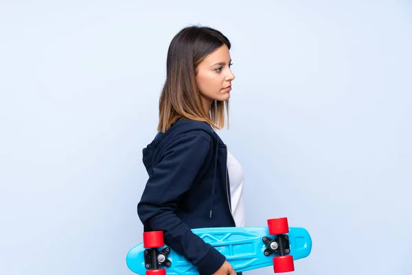 年轻女子 背向滑板的孤立的蓝色背景 — 图库照片