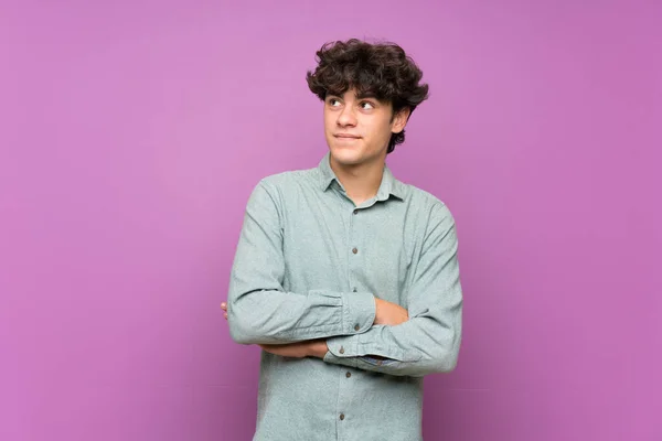 Young man over isolated purple wall looking up while smiling