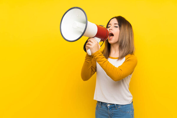 Pretty young woman over isolated yellow wall shouting through a megaphone