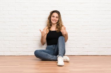 Genç sarışın kadın jest kadar bir başparmak vererek katta oturan