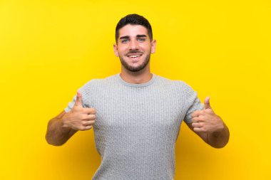 Izole sarı arka plan üzerinde genç yakışıklı adam jest kadar bir başparmak veren
