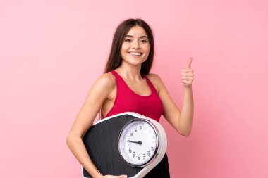 Tecrit edilmiş pembe arka plan üzerinde tartı makinesi olan genç ve güzel bir kız.