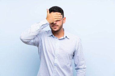 Kafkas yakışıklı adam izole edilmiş mavi arka planda gözlerini elleriyle kapatıyor.