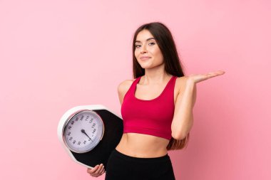 Tartı makinesi ile izole edilmiş pembe arka planda tartı makinesiyle güzel bir genç kız.
