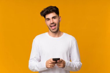 İzole edilmiş turuncu arka planı olan genç adam şaşırdı ve bir mesaj gönderiyor.