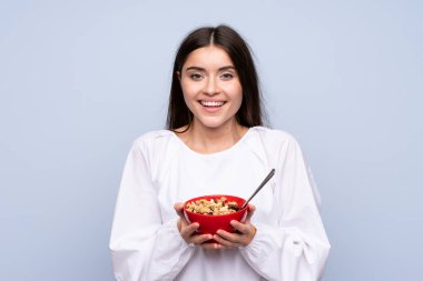 Bir kase mısır gevreği taşıyan soyutlanmış mavi arka planda genç bir kadın.