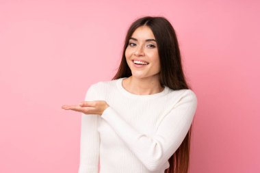 Soyutlanmış pembe arka planda genç bir kadın. Davet edilmek için ellerini yana uzatıyor.