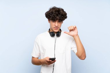 Mobil müzik dinleyen genç adam mavi duvarın üzerinde gururlu ve kendini beğenmiş.