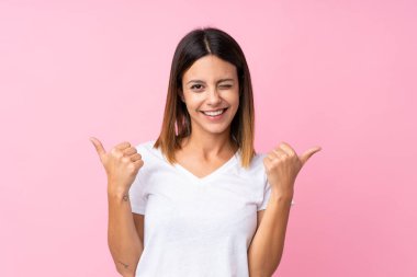 Soyutlanmış pembe bir geçmişi olan genç bir kadın. Baş parmakları havada ve gülümsüyor.