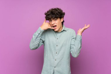 Mor duvardan izole olmuş genç bir adam telefon jesti yapıyor ve şüpheci