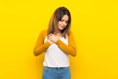 Güzel bir genç kadın, izole edilmiş sarı duvarın üzerinde, kalbinde bir ağrı var.