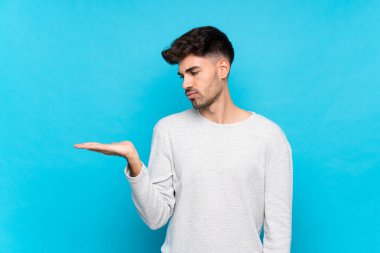 İzole edilmiş mavi arkaplan üzerinde genç bir adam kopyalama alanını şüpheyle tutuyor