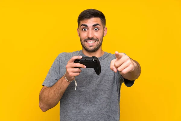 Joven hombre guapo jugando con un controlador de videojuegos sobre fondo amarillo aislado —  Fotos de Stock