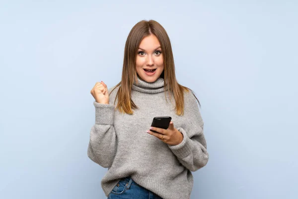 Teenager Mädchen Mit Pullover Über Isoliertem Blauem Hintergrund Mit Handy — Stockfoto