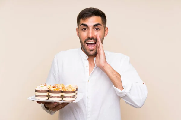 Hombre Guapo Sosteniendo Pastel Magdalenas Sobre Fondo Aislado Con Sorpresa — Foto de Stock