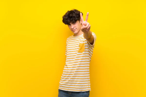 Junger Mann Über Isolierte Gelbe Mauer Lächelt Und Zeigt Siegeszeichen — Stockfoto