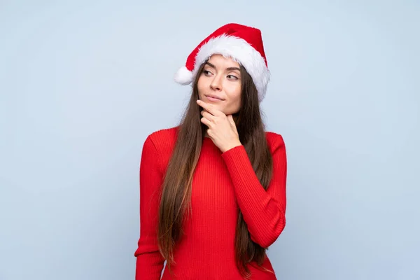 戴著圣诞帽的女孩在孤零零的蓝色背景下思考着一个想法 — 图库照片