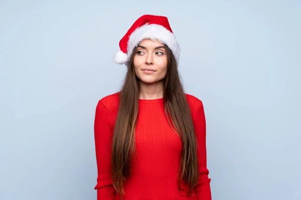 戴着圣诞礼帽站在孤零零的蓝色背景上向旁边看的女孩 — 图库照片