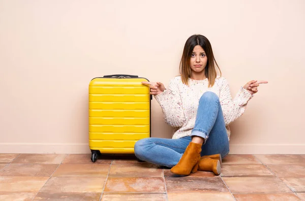 旅行妇女 提着手提箱坐在地板上 指向有疑问的侧面 — 图库照片