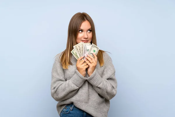 Izole mavi arka plan üzerinde kazak ile genç kız çok para alarak