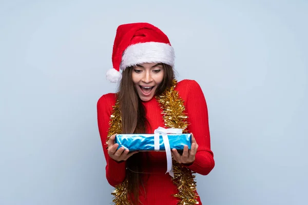 Menina Com Chapéu Natal Segurando Presente Sobre Fundo Azul Isolado — Fotografia de Stock